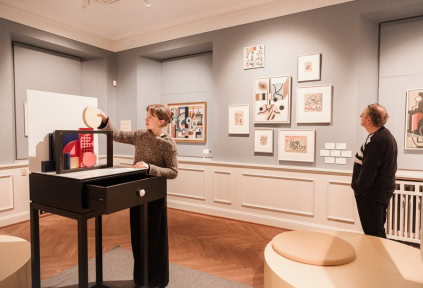 A young woman is creating an artwork with various figures, while a man is admiring the artwork of the artist Franciska Clausen