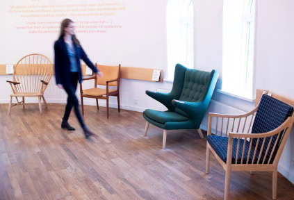 A young woman is walking past the many chairs designed by Hans J. Wegner.