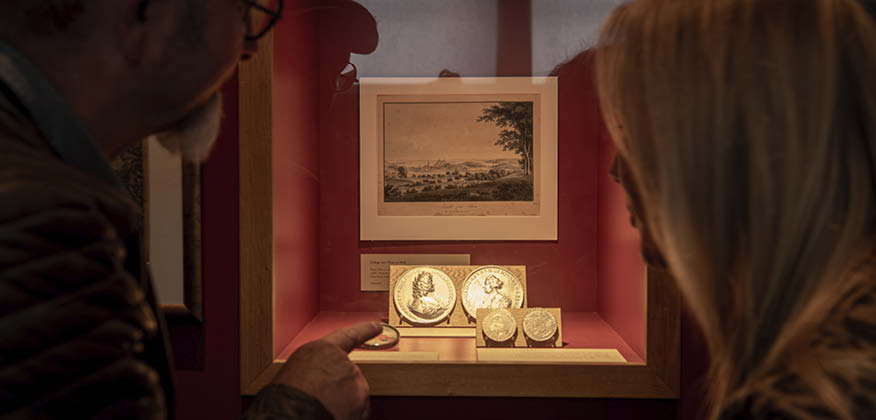 Mand og kvinde står ved en udstillingsmontra med mønter i.