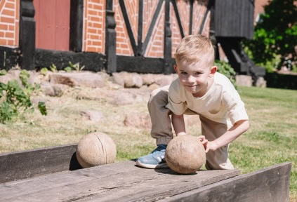 A young boy is playing a traditional skittles game at the Open-Air Museum in Haderslev