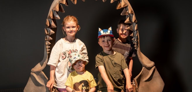 Four children are standing inside a replica of the jaws of the Megalodon shark