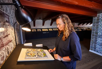 A woman is examining a collection of Dutch tiles on display