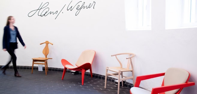 A woman is passing by the chairs designed by Hans J. Wegner
