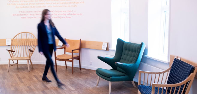 Eine Frau geht an die vielen Stühle von Hans J. Wegner vorbei