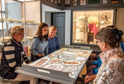 Leute sitzen um einen Tisch und schauen sich in der Ausstellung im Schloss Sonderburg einen digitalen Bildschirm mit einem Kuchen an