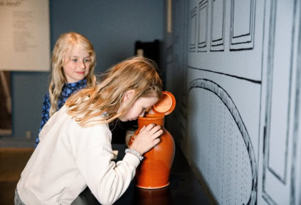 A girl is smelling something inside a ceramic pot