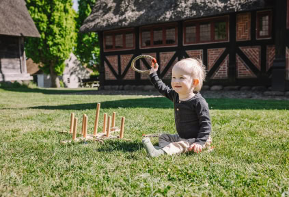 A baby boy is sitting on the grass with a toy at the Open-Air Museum in Haderslev
