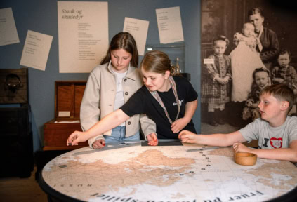 Three children are playing a board game in the exhibition at Cultural History Aabenraa