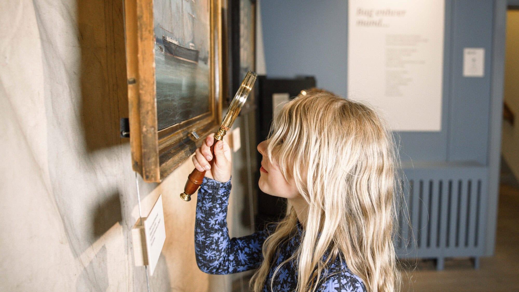 Pige står med lup foran et skibsportræt der hænger på Kulturhistorie Aabenraa