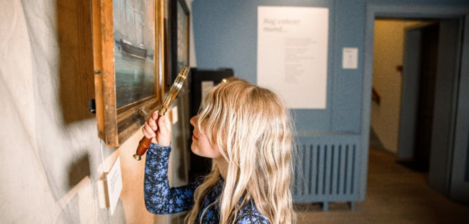 A girl is looking at a portrait of a ship with a loupe
