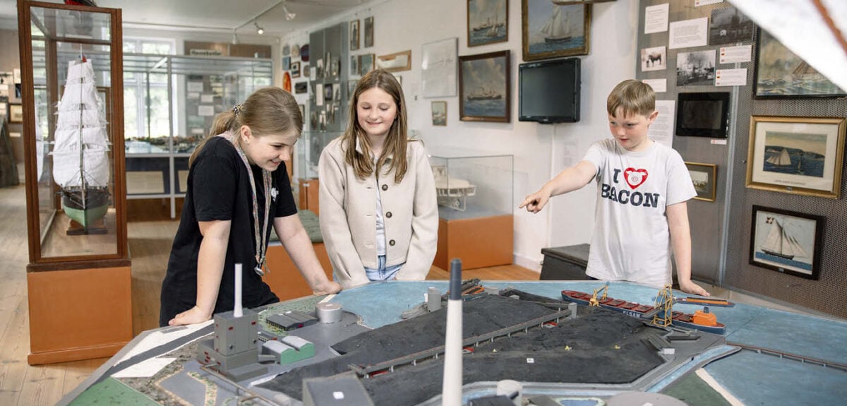 to piger og en dreng står ved model af aabenraa havn.